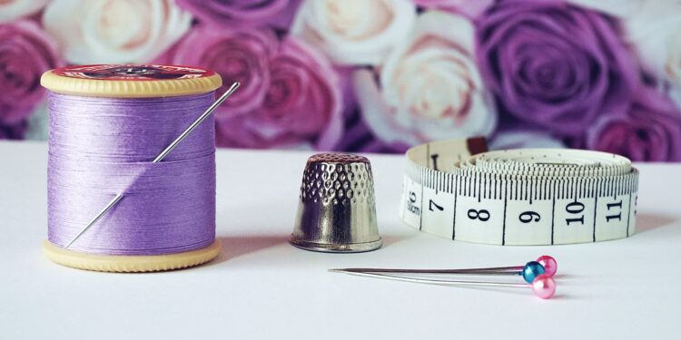 spool of purple thread near needle thimble and measuring tape