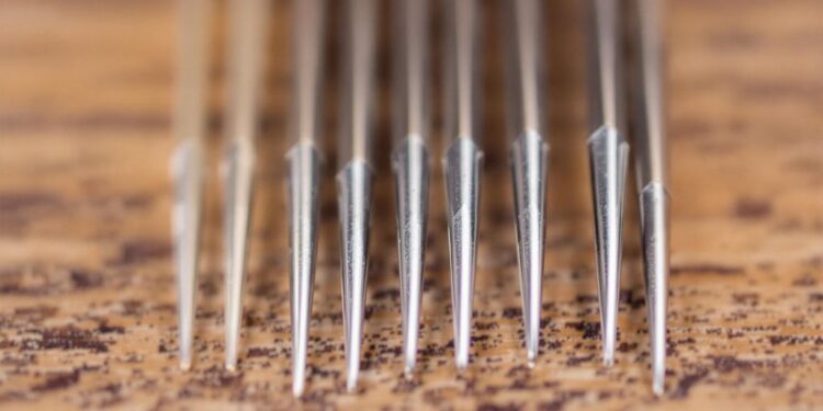 Assorted sewing machine needles on a wooden surface.
